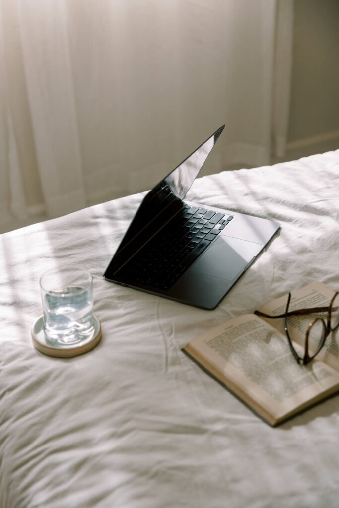 diy website on a laptop, sitting on a bed with a book and glasses