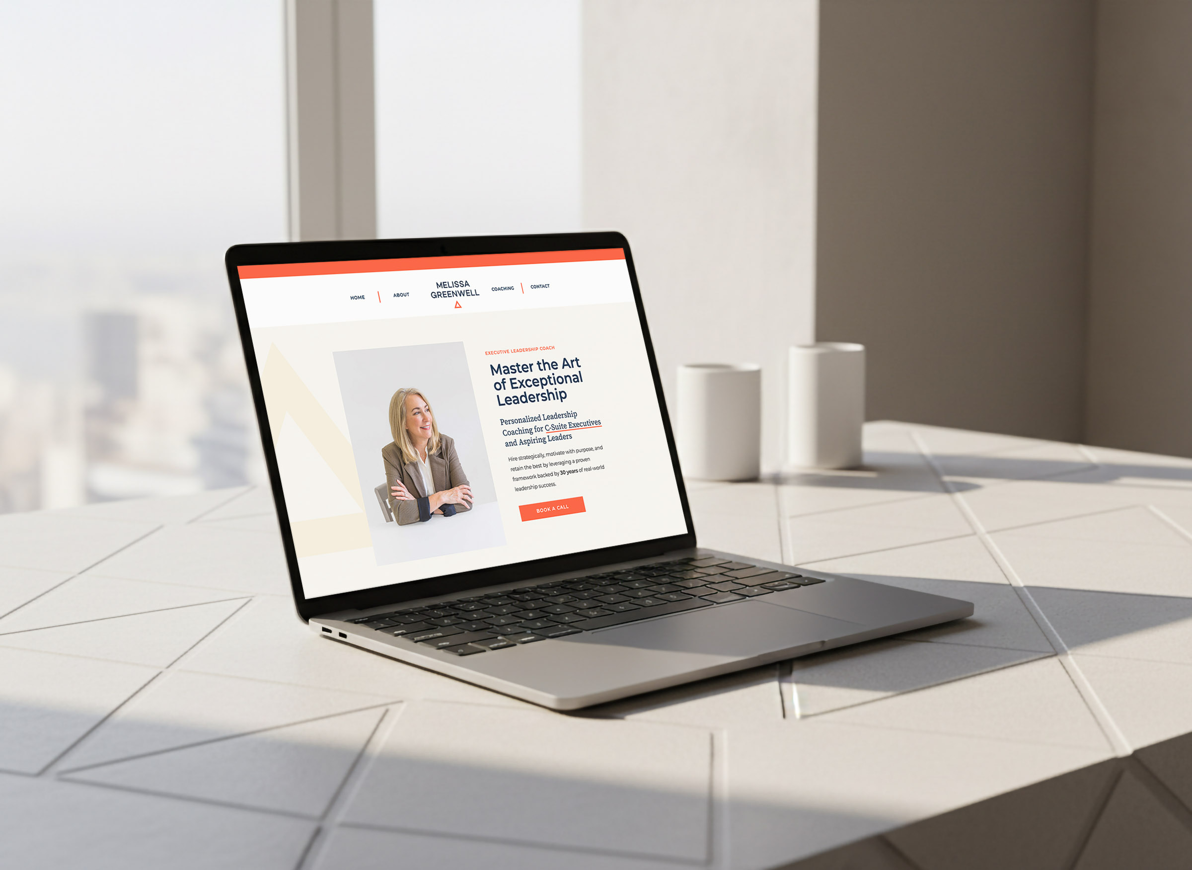 melissa greenwell, executive leadership coach, website design mocked up on a modern laptop sitting on a modern desk overlooking a window with a cityscape in the background
